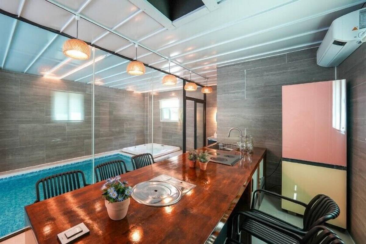 Uma sala de conferências moderna com divisória de vidro, mesa de madeira, cadeiras, uma pequena piscina e iluminação pendente.