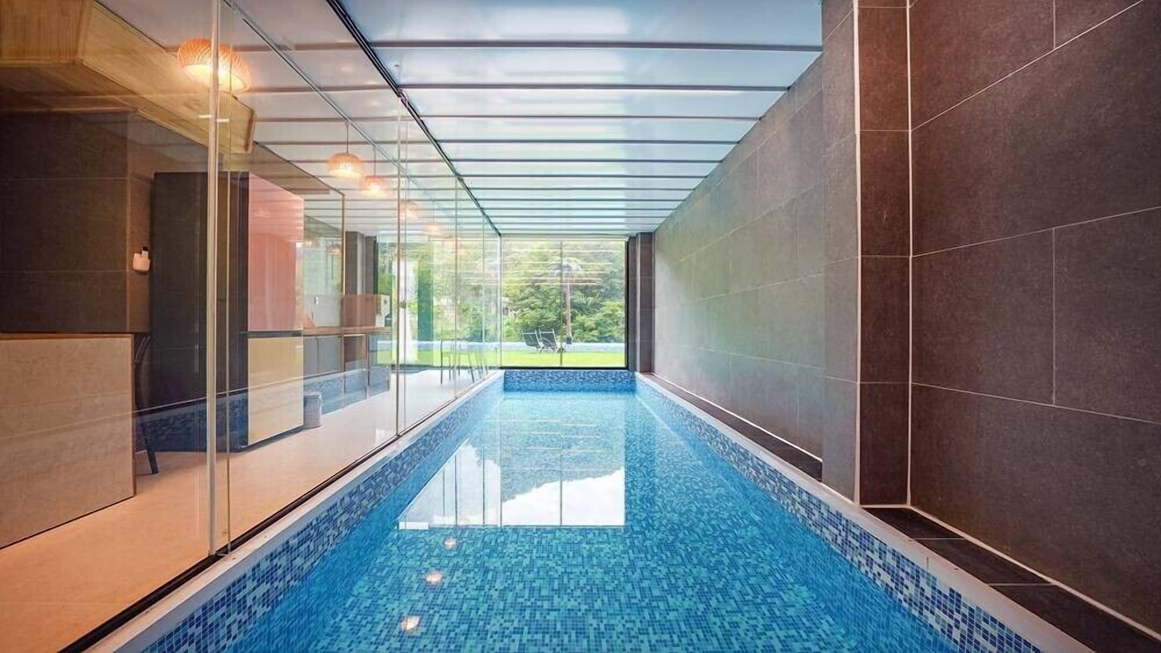 Una piscina interior con paredes de vidrio transparente, piso de baldosas y vistas al exterior.
