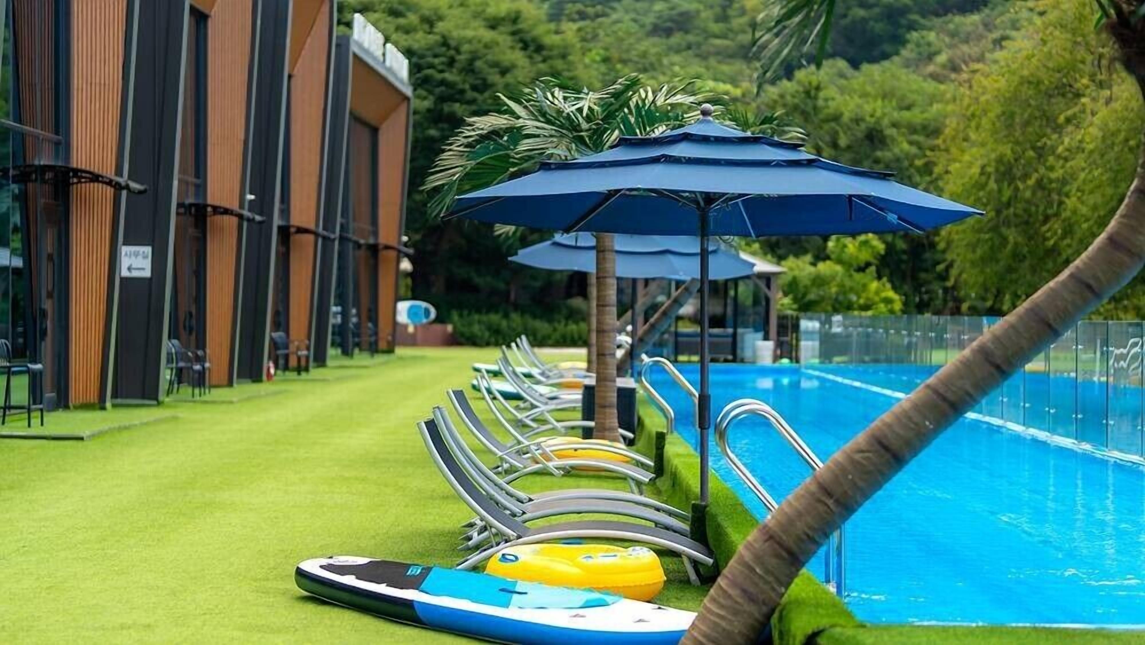 A pool area with lounge chairs and umbrellas, surrounded by a building with vertical wooden slats.