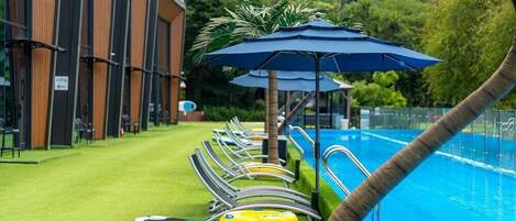 A pool area with lounge chairs and umbrellas, surrounded by a building with vertical wooden slats.