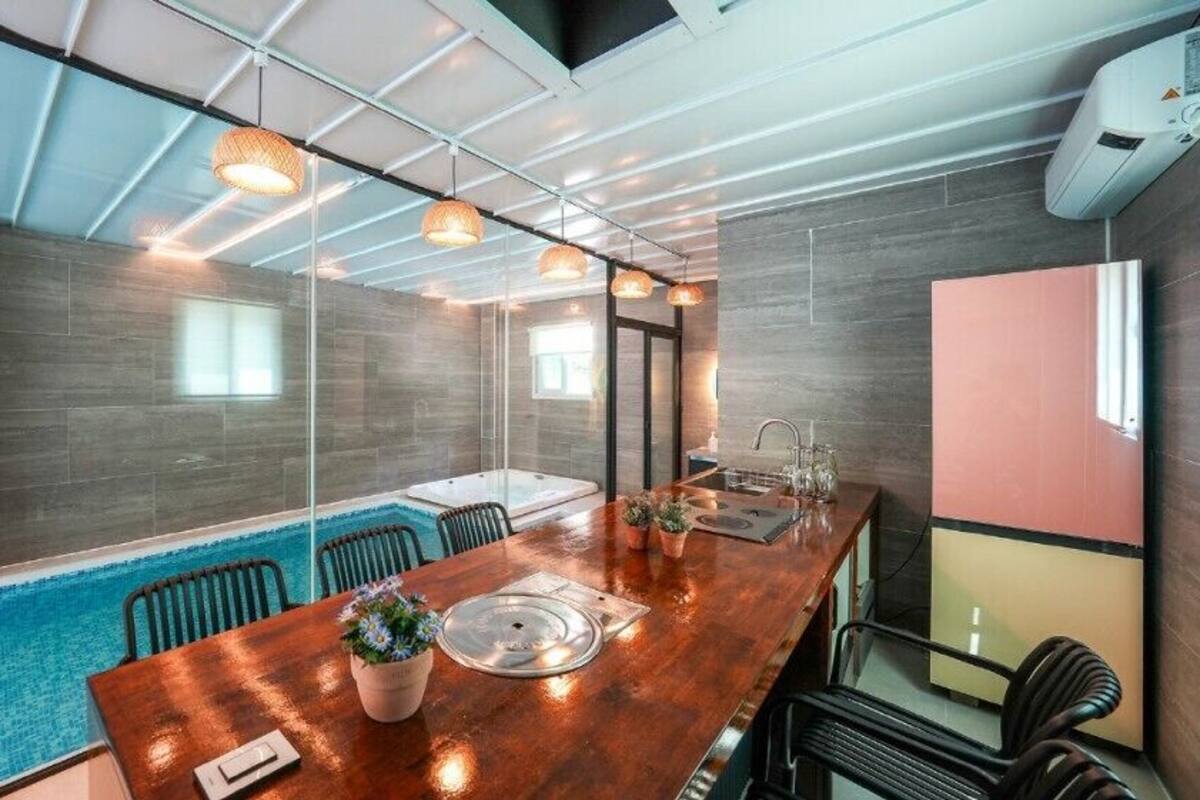 A modern conference room with a glass partition, a wooden table, chairs, a small pool, and pendant lighting.