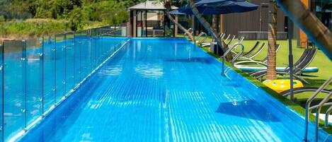 A clear blue pool with a glass barrier, lounge chairs, and umbrellas.