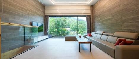 A modern living room with a sofa, a coffee table, and a TV mounted on a glass wall.