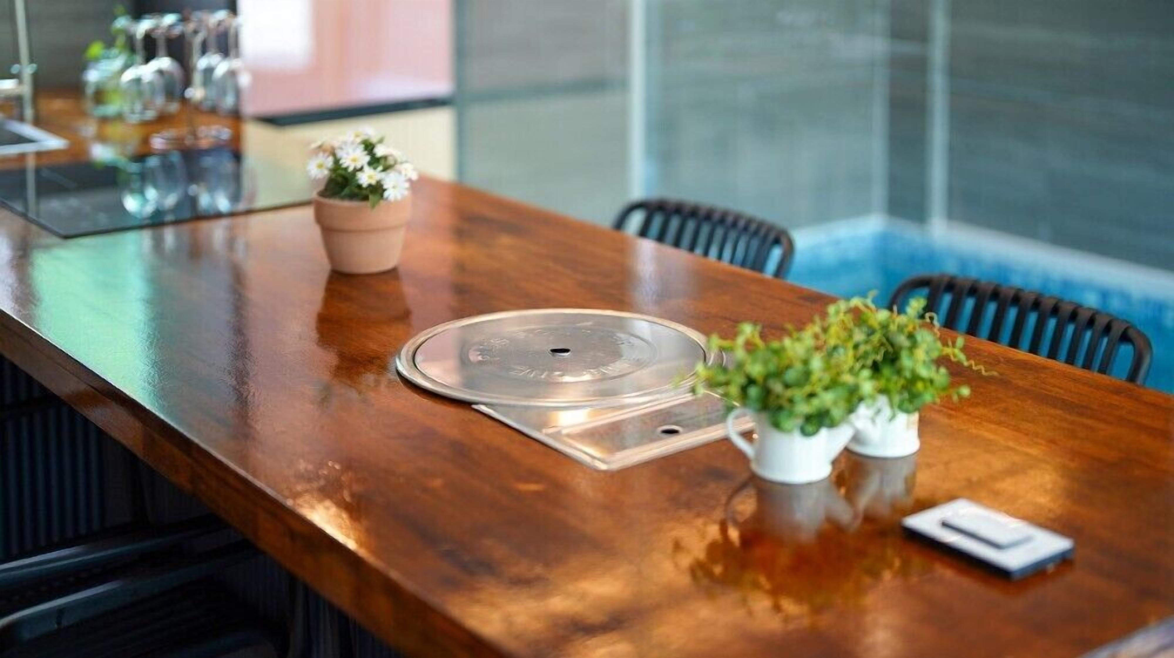 Una mesa de conferencias de madera con una bandeja metálica, plantas en macetas y un teléfono inteligente.