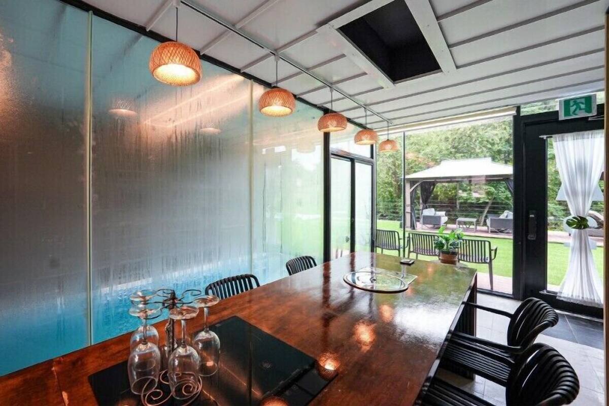 A conference room with a long table, chairs, and a glass partition. There are hanging lights and a view of the outdoors.