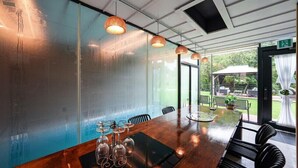 A conference room with a long table, chairs, and a glass partition. There are hanging lights and a view of the outdoors. - Metaverse Pension (Gapyeong)