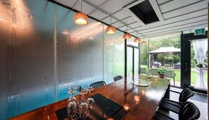 A conference room with a long table, chairs, and a glass partition. There are hanging lights and a view of the outdoors. - Metaverse Pension (Gapyeong)