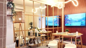 Ein modernes Wohnzimmer mit einem Holzesstisch, weiß gepolsterten Sitzmöbeln und einem großen Flachbildfernseher an der Wand.