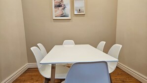 Una habitación con una mesa y sillas blancas, suelo de madera y dos cuadros en la pared.
