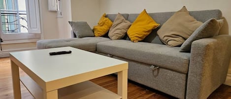 Ein Wohnzimmer mit einem grauen Sofa, gelben und beigen Kissen, einem weißen Couchtisch und Holzböden.
