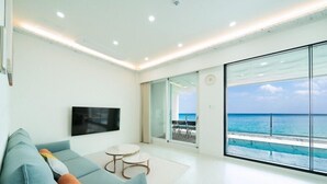 Una sala de estar moderna con un sofá, un televisor de pantalla plana y un balcón con vistas al océano.