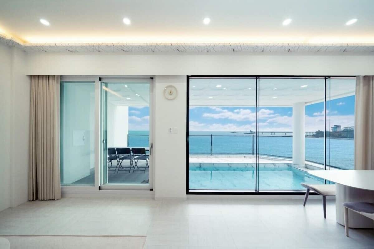Ein modernes Zimmer mit einer großen Schiebeglasdoor zu einem Balkon mit Pool und Meerblick.
