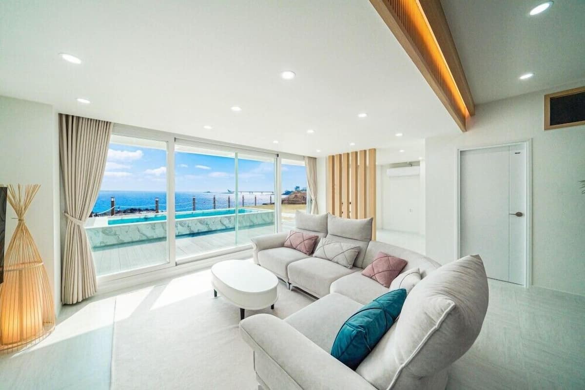 Ein modernes Wohnzimmer mit einer Couch, einem Couchtisch und Blick auf einen Pool und das Meer.