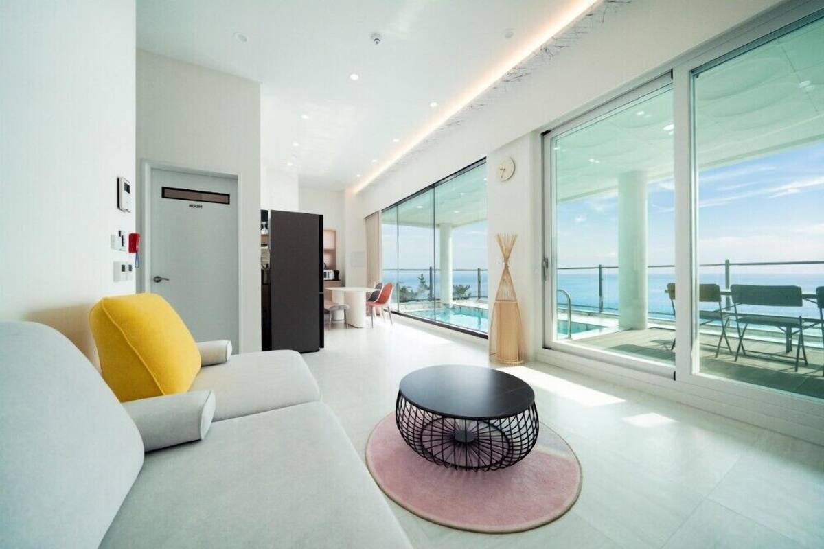 Ein modernes Wohnzimmer mit Sofa, rundem Tisch und Meerblick durch große Fenster.