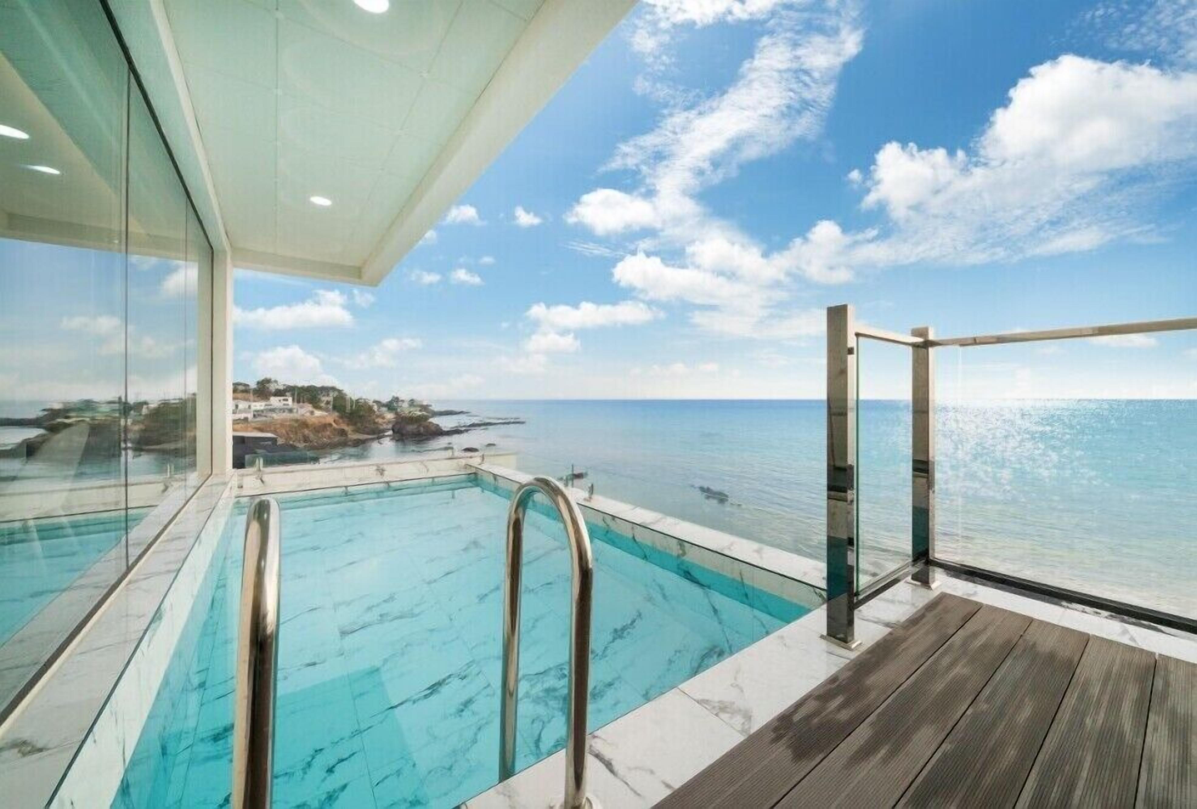 A pool with a clear view of the ocean and a wooden deck.