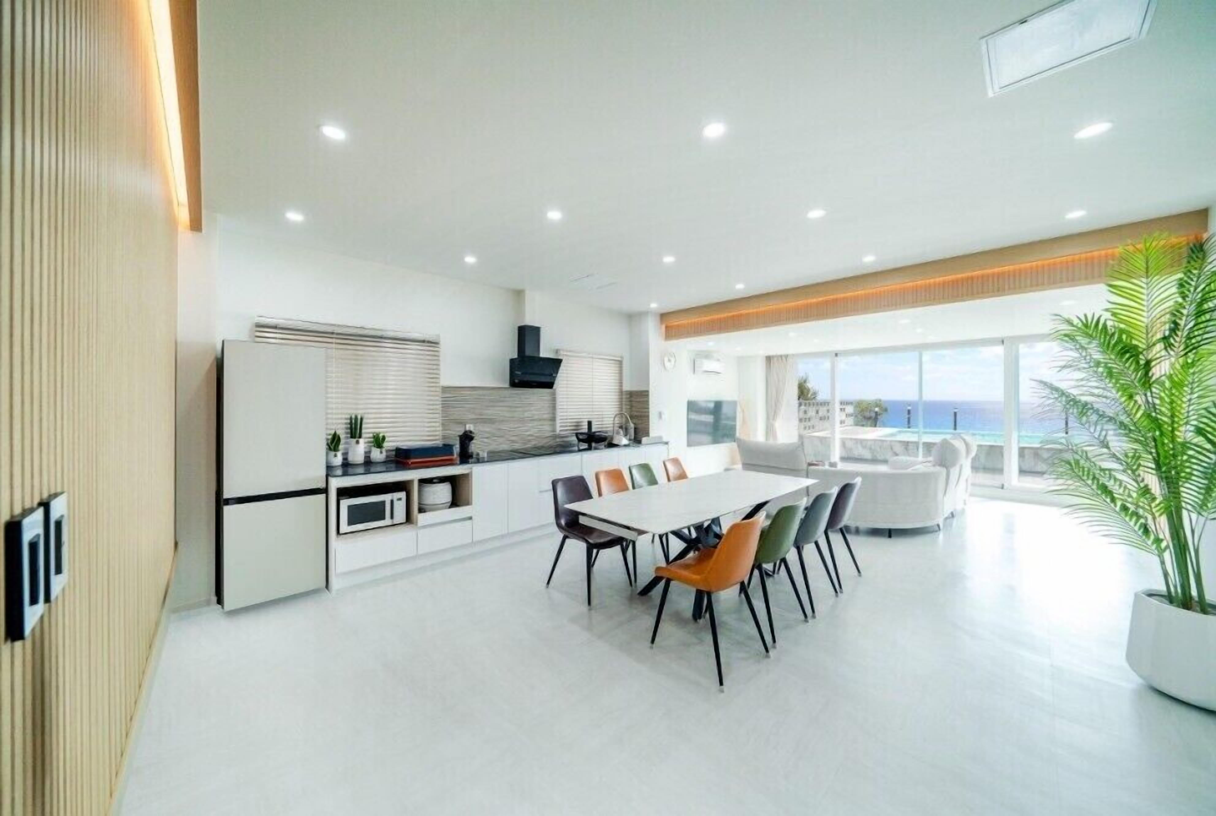 A modern kitchen with a dining area, large windows, and a view of the ocean.