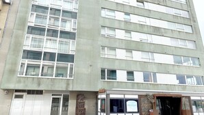 Un immeuble à plusieurs étages doté d’une architecture moderne, avec une entrée au niveau du sol caractérisée par une façade en verre et une enseigne indiquant la présence d’un restaurant.