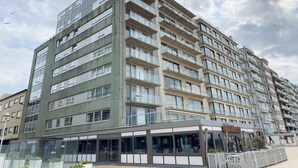 Un immeuble résidentiel à plusieurs étages, doté de balcons, de grandes fenêtres et d’une entrée au niveau du sol.