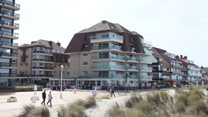 Un hôtel situé en bord de mer, doté de nombreux balcons, d’une promenade de sable et offrant une vue sur un ciel dégagé.