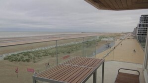 Un balcon donnant sur une plage, avec une table et une rambarde.