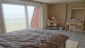 Une chambre avec un grand lit, un bureau, une chaise et une vue sur la plage.