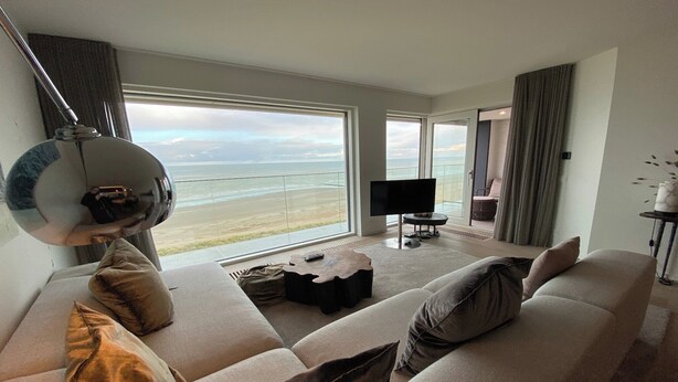 A modern living room with a large window, a flat-screen TV, and a sofa with cushions.