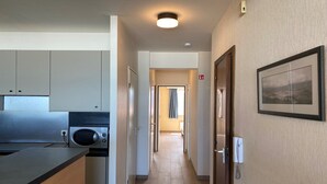 Un couloir étroit, avec une kitchenette sur la gauche, une porte dotée d’un système de verrouillage à carte magnétique sur la droite, et un tableau encadré au mur.
