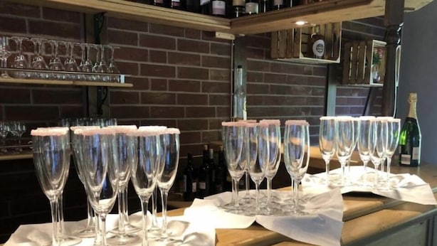 A bar area with multiple glasses lined up on a counter, a brick wall in the background, and bottles of wine on shelves. - Hotel Restaurant Hillmers Hoff (Undeloh)
