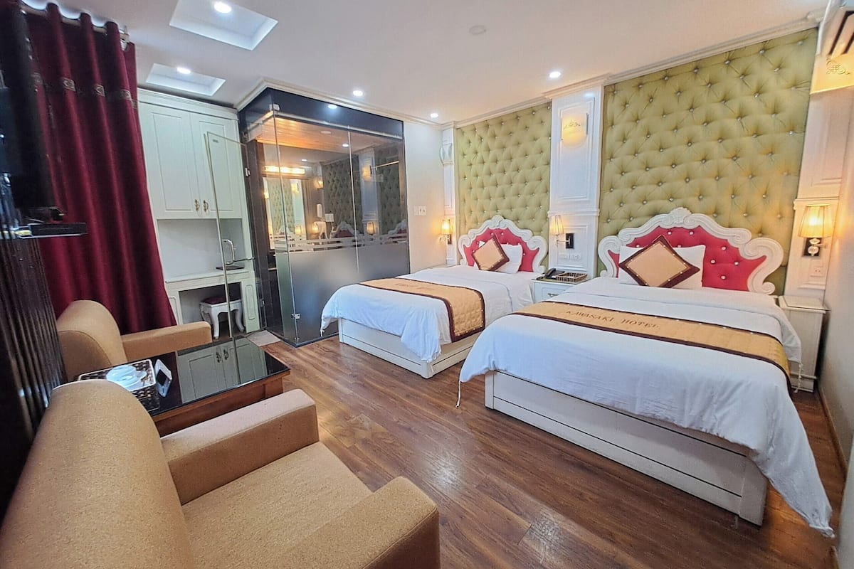 Une chambre d’hôtel avec deux lits, un coin salon, un miroir et une petite table.