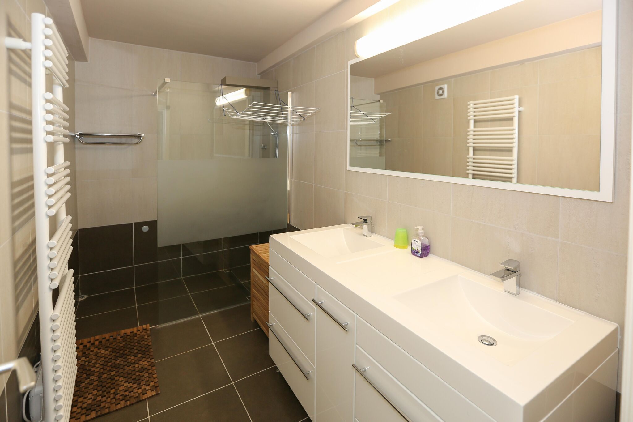 Une salle de bain moderne dotée d’un grand miroir, de deux vasques et d’une cabine de douche en verre.