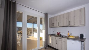 A modern kitchen with a sliding glass door leading to a balcony, a white refrigerator, and wooden cabinets. - Myrsini's Luxury Suites (Mykonos)