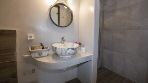 A bathroom with a marble sink, a mirror, and a shower. - Myrsini's Luxury Suites (Mykonos)