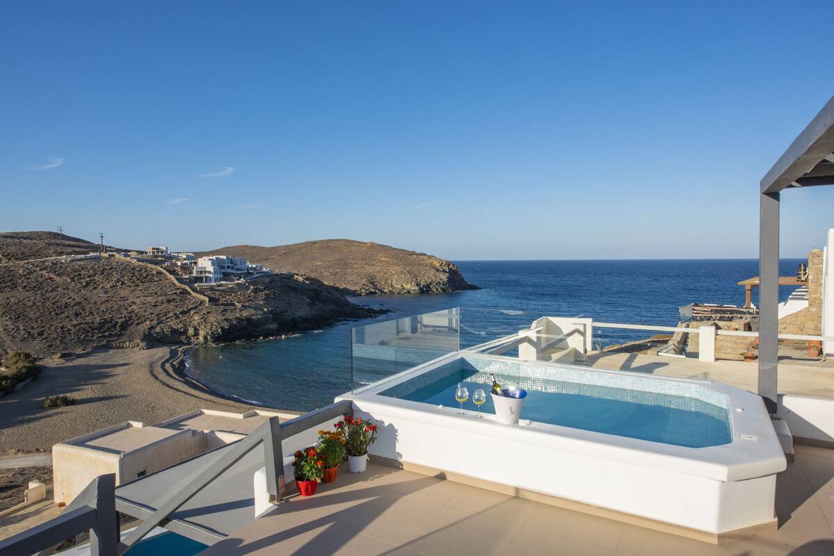 A pool area with a view of the sea, a beach, and a hilly landscape.