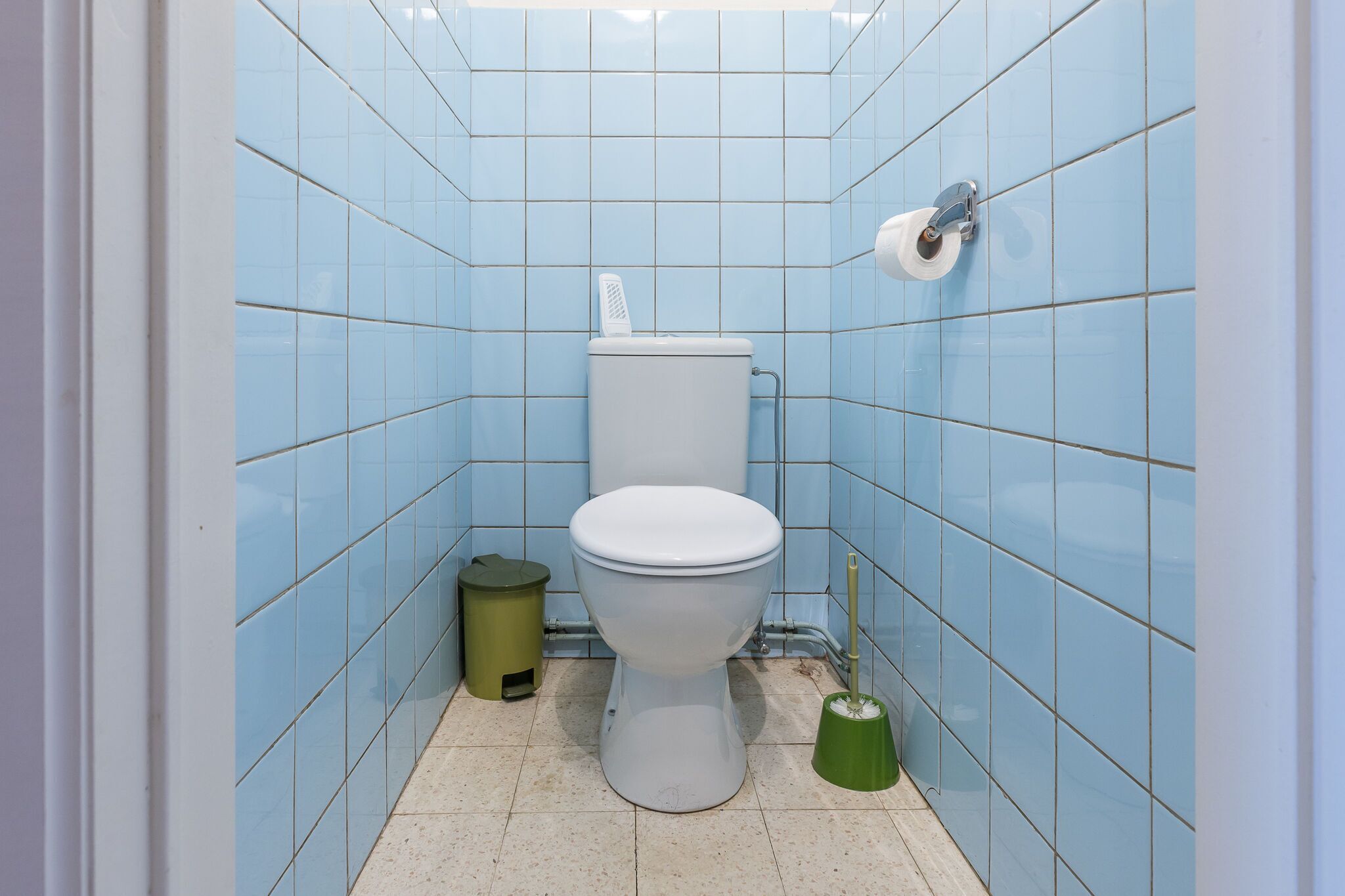 Un baño pequeño con azulejos, un inodoro, un cubo de basura y un cepillo para el inodoro.