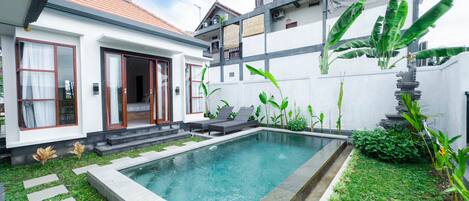 A modern house with a swimming pool, a covered patio, and lush greenery.
