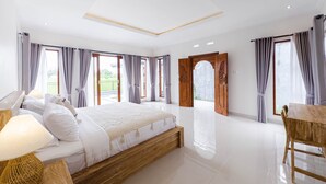 Une chambre spacieuse avec un grand lit, une tête de lit en bois et une vue sur l’extérieur grâce à une porte-fenêtre coulissante.