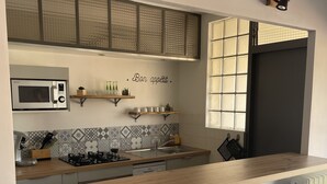A modern kitchen with a wooden countertop, two bar stools, a microwave, and a window with frosted glass panels.