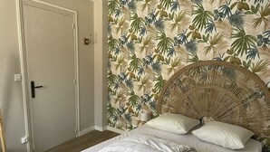 A bedroom with a bed, a rattan headboard, and a tropical leaf-patterned wallpaper.