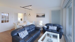 Una sala de estar moderna con dos sofás de cuero negro, una mesa de centro blanca y un comedor con mesa y sillas blancas.