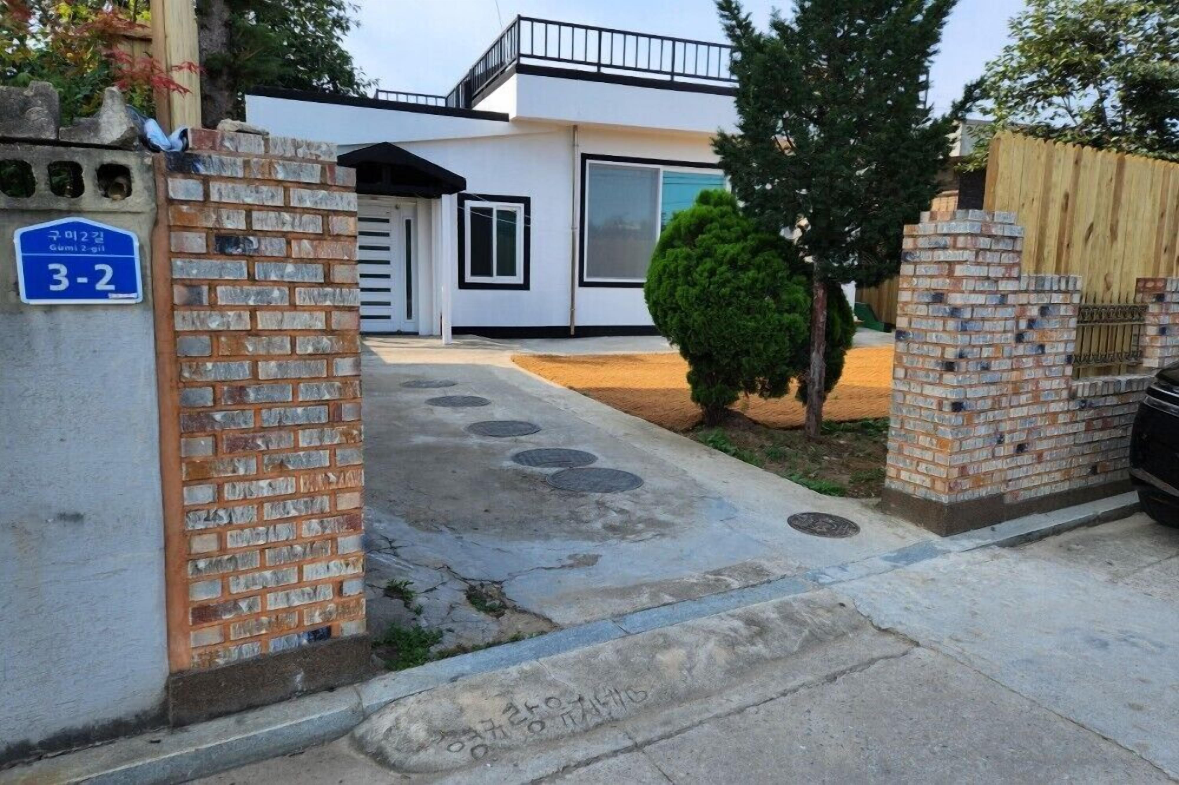 A modern two-story house with a brick gate and a blue sign indicating the address.