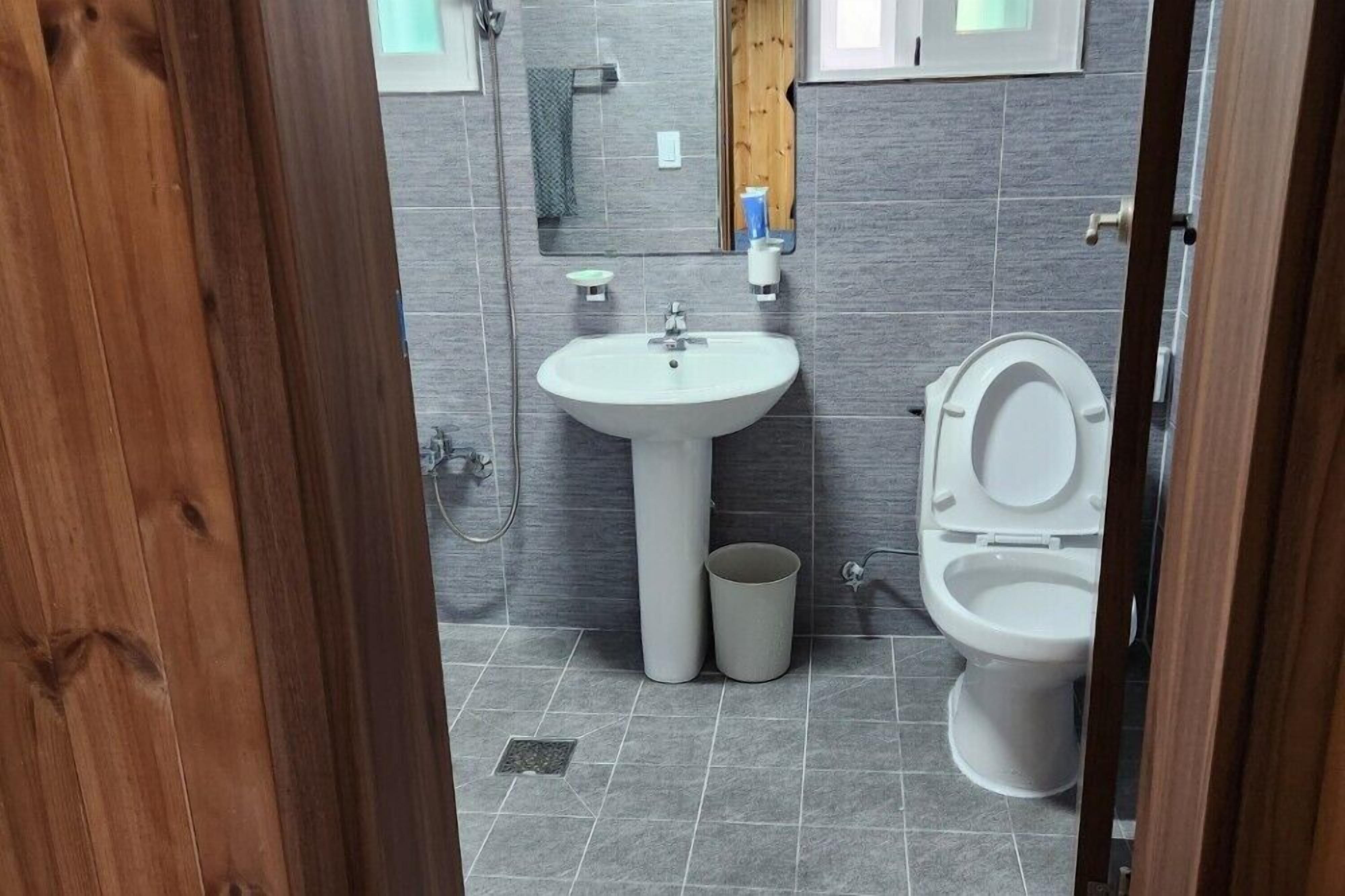 Un baño con lavamanos blanco, inodoro y un pequeño cubo de basura.