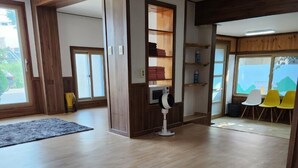 Una habitación amplia con suelo de madera, una estantería empotrada, un ventilador de pie y vistas a través de un ventanal grande.