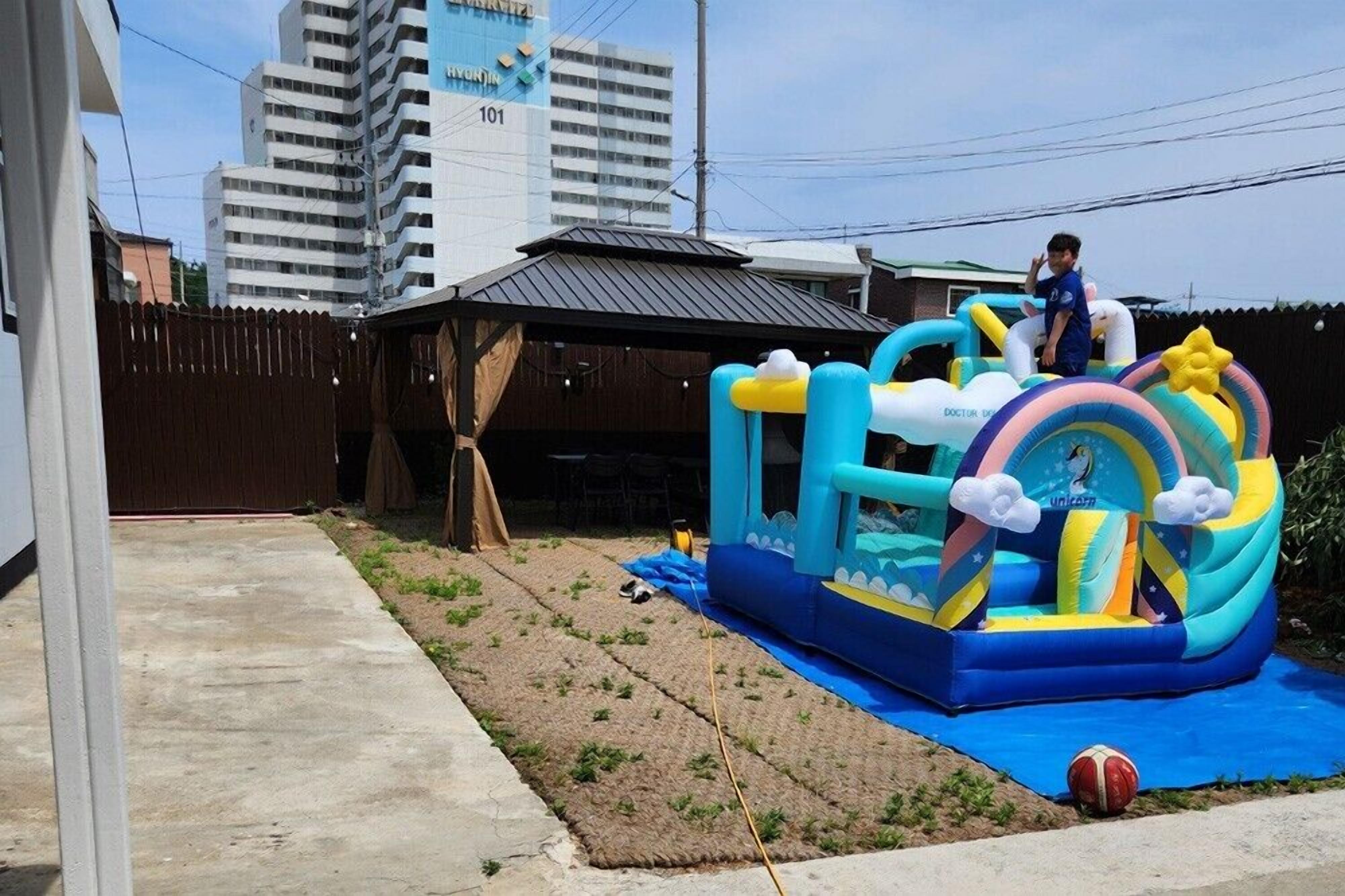 Uma estrutura de brinquedo inflável em formato de unicórnio em um quintal com um pátio de concreto e cerca de madeira.