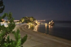 A beach with a curved shoreline, trees, and a distant cityscape. - dong hae ae pension (Donghae)