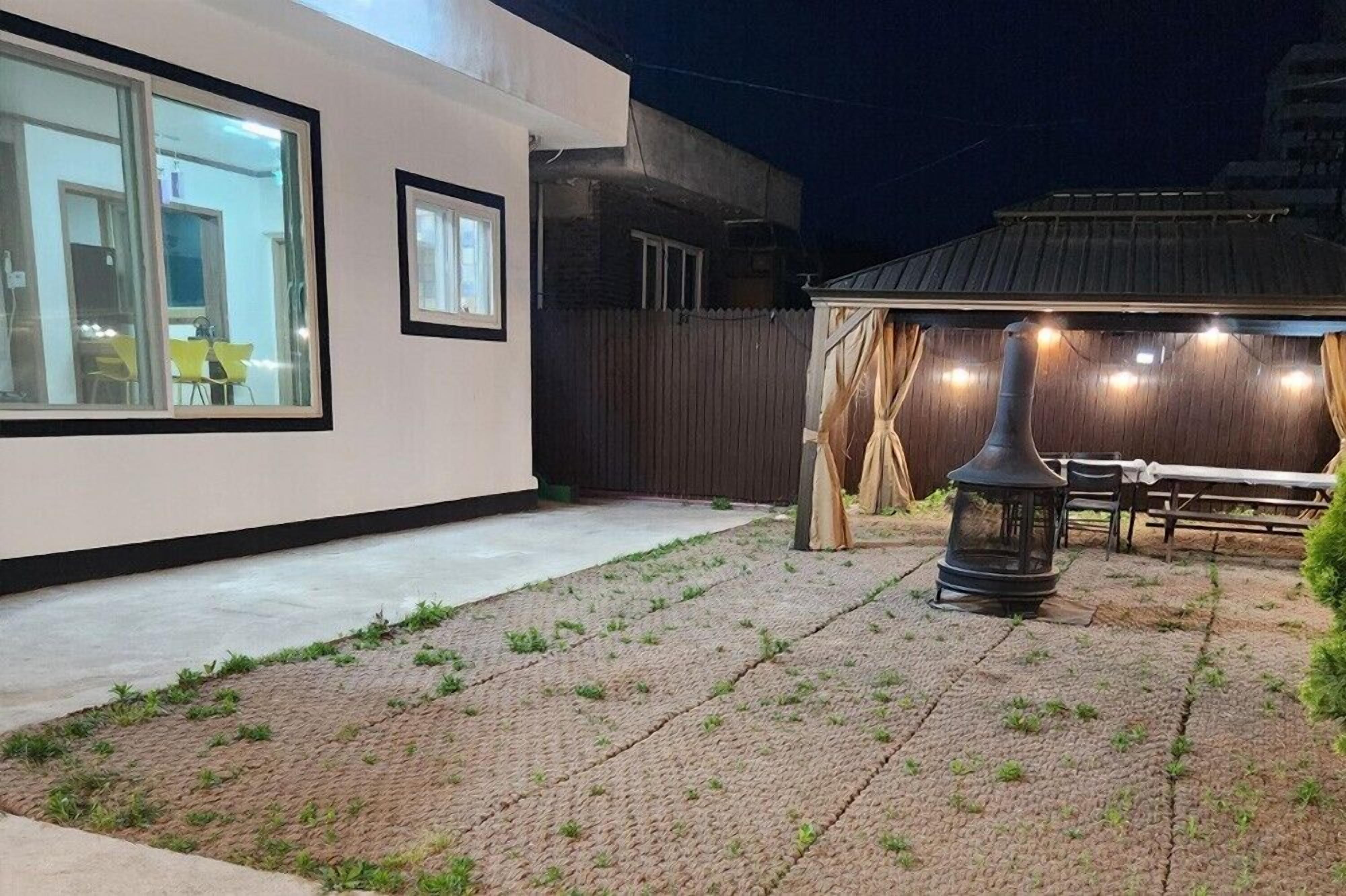 A modern house with a paved backyard, a wooden fence, and a patio area with a table and chairs.
