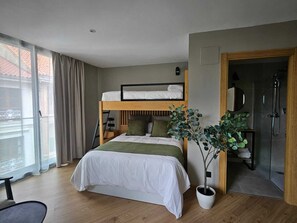 Une chambre d’hôtel moderne équipée d’un lit superposé, d’une plante en pot, d’un bureau et d’un espace douche.