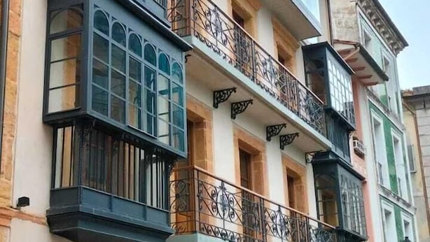 Un edificio de varios pisos con balcones, ventanas amplias y suelo mojado, indicando lluvia reciente.