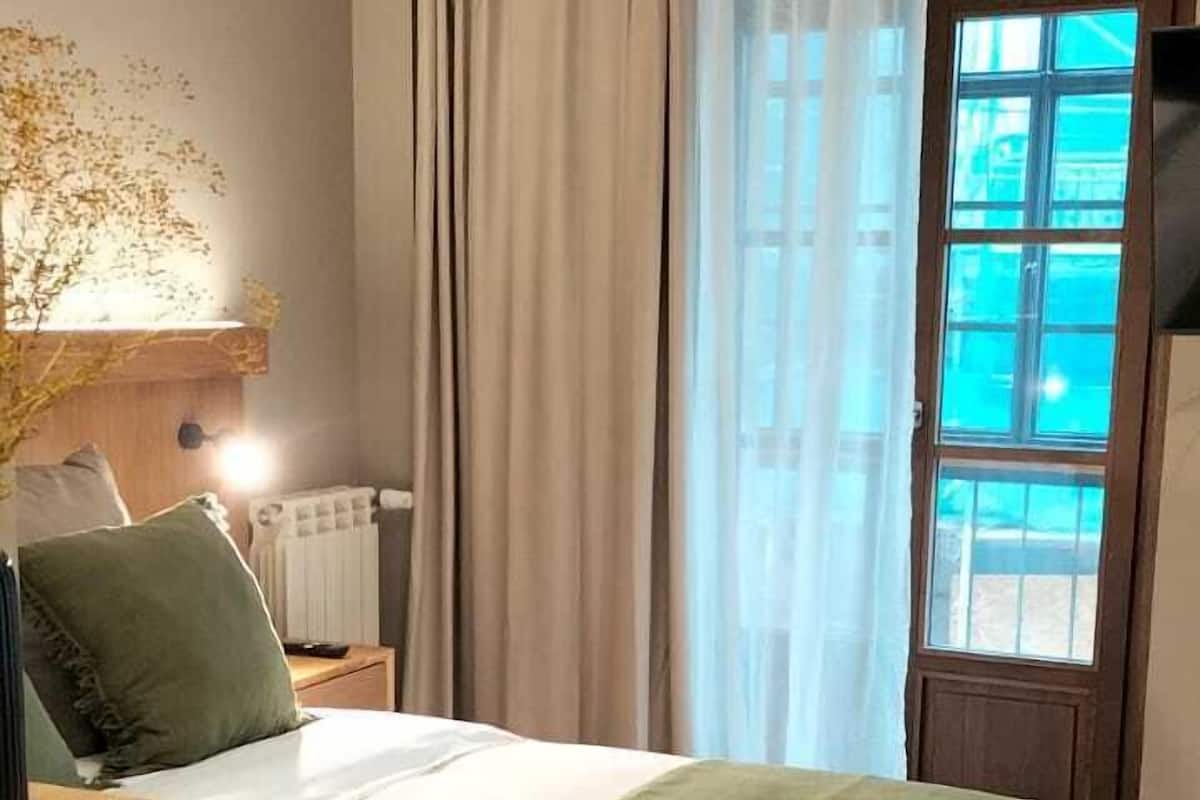Une chambre d’hôtel avec un lit, un bureau en bois, une lampe et une vue sur l’extérieur par une fenêtre.