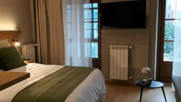 Une chambre d’hôtel comprenant un lit, une table de chevet, un téléviseur fixé au mur, un radiateur et une fenêtre avec des rideaux.