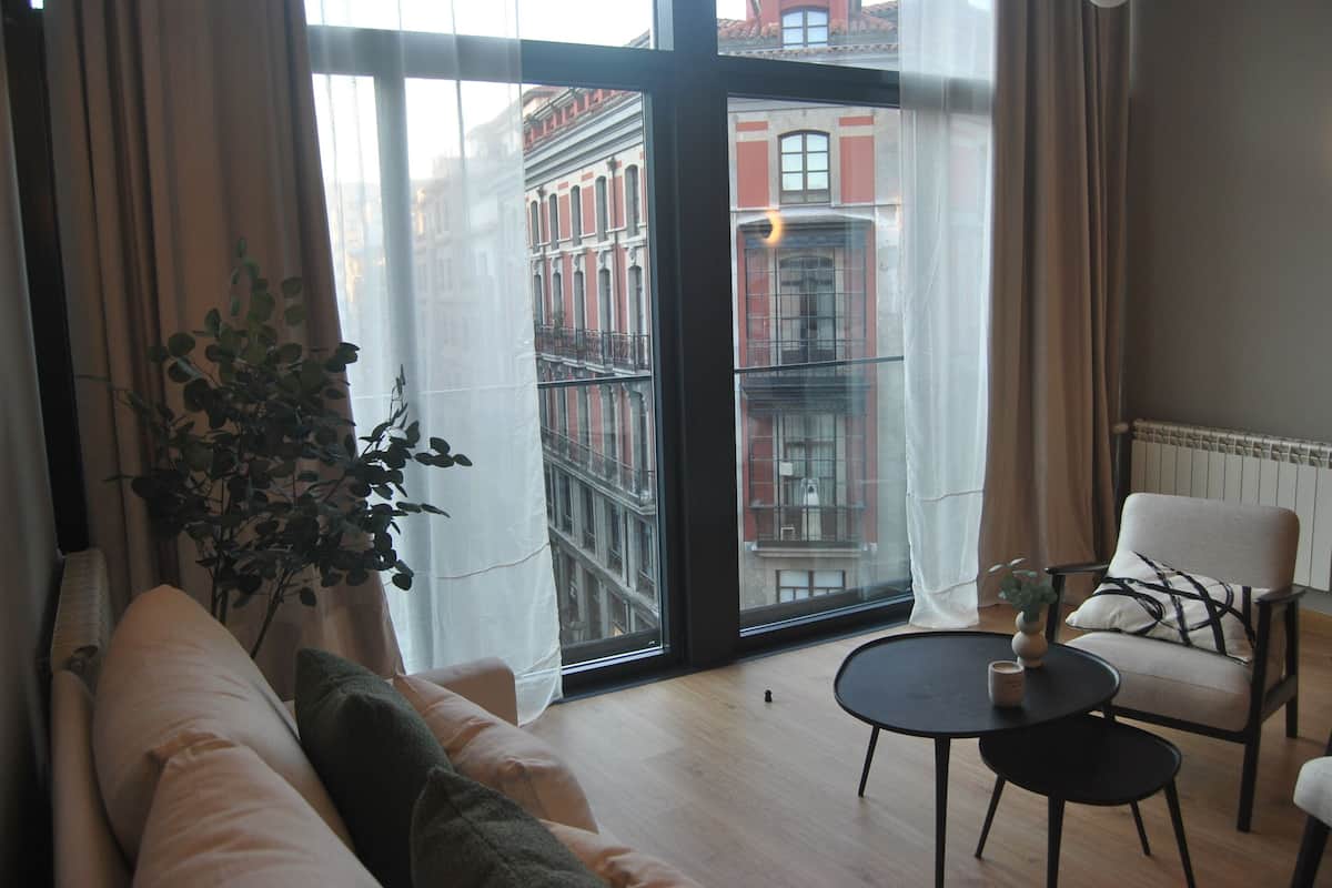 Un salon moderne avec une grande fenêtre, un canapé, un fauteuil et une petite table.